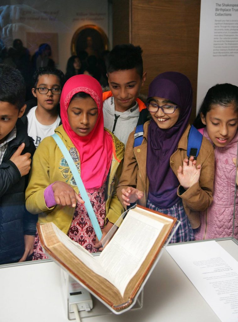 A group of children look at a book within a glass cabinet
