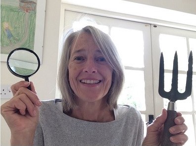 A female volunteer holds up her magnifying glass and gardening fork