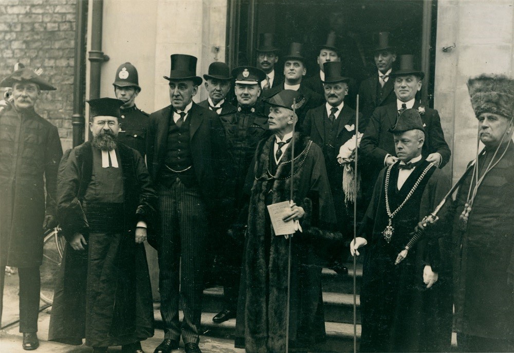 A black and white photograph of men outside a synagogue, some wearing top hats and others in religious garments