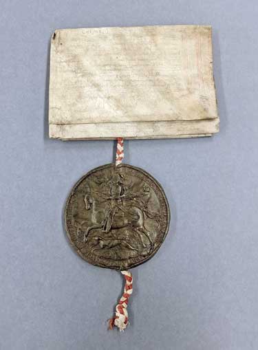 A folded sheet of paper with a large brown wax circle with a king on horseback imprinted on it attached with string.