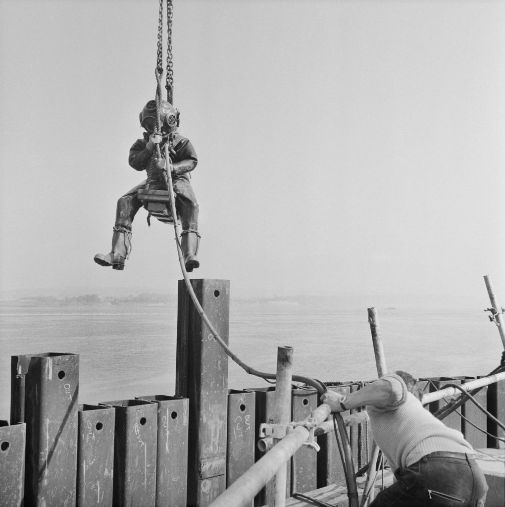 A person is metal scuba gear hangs from a rope above the water