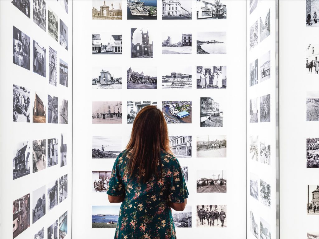 A woman standing a brightly lit room with archives images arranged in grids on the walls