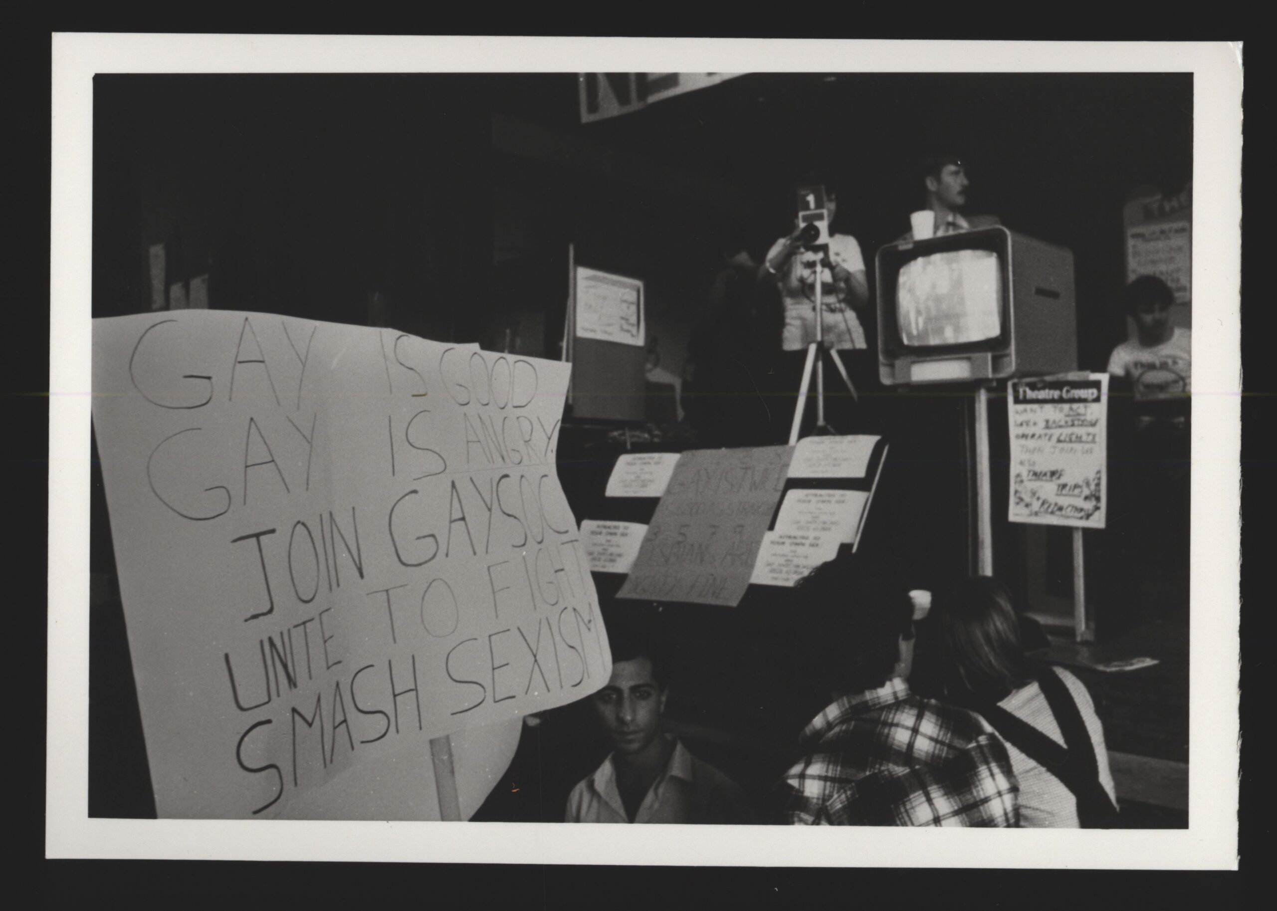 A black and white photo of a protest including the banner 'Gay is good'