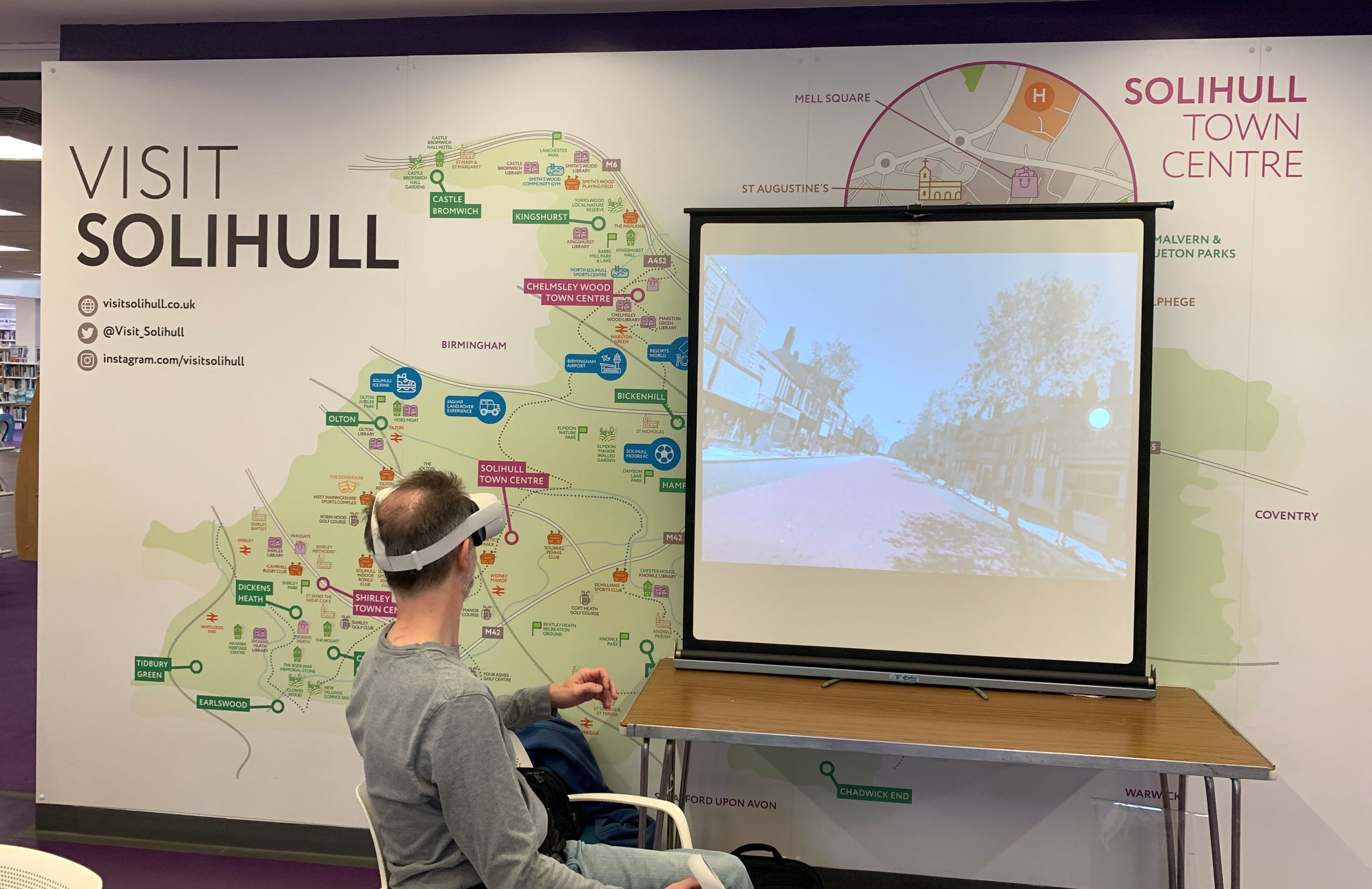 A man using a virtual reality headset with his view projected on a screen in front of a map of Solihull