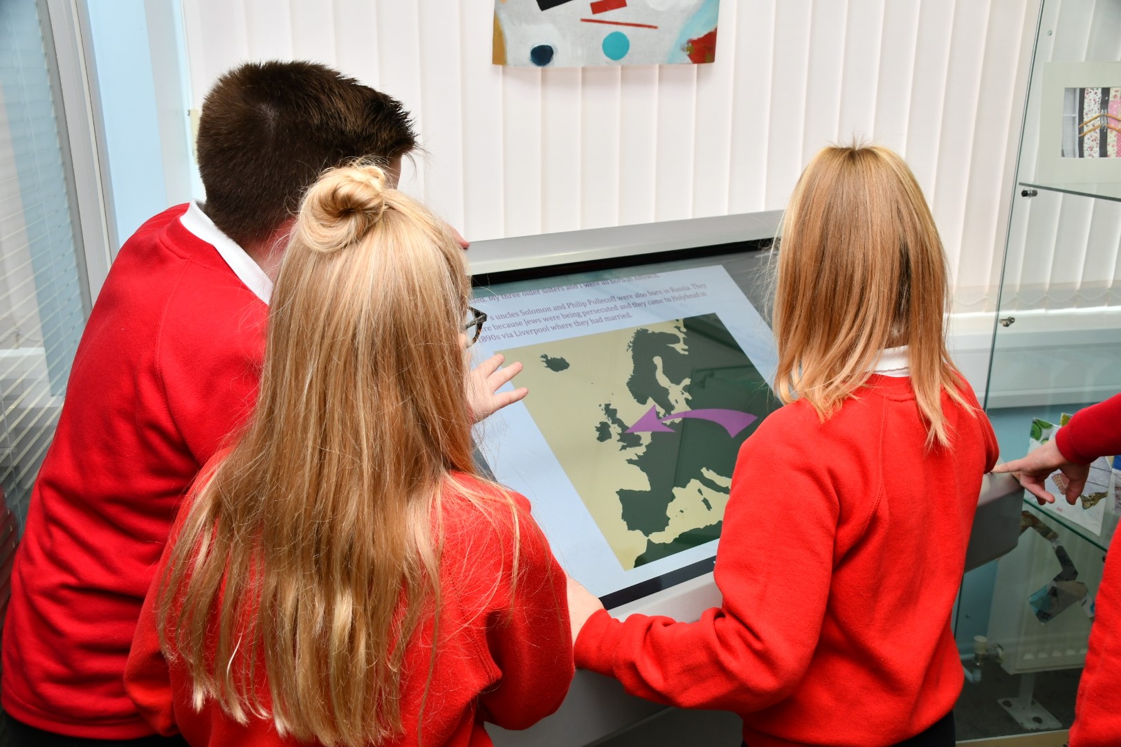 Three school children touching an interactive screen in an exhibition