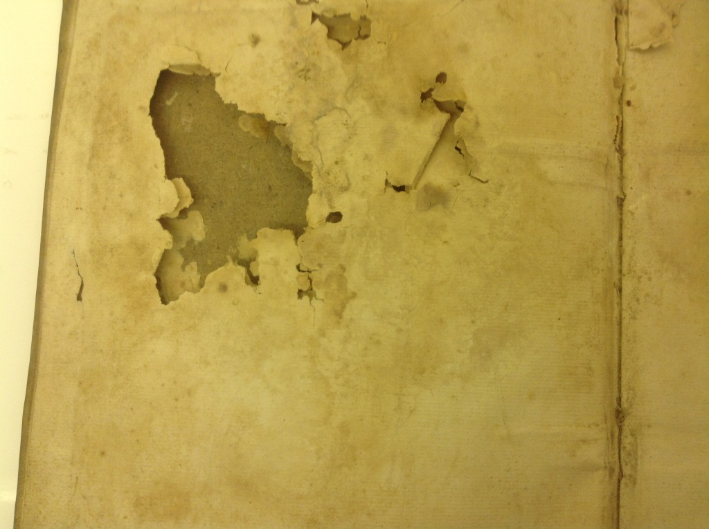 A yellowed paper document, with large holes on the top left part of it. The holes extend through several leaves of paper.