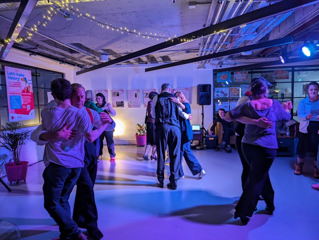 A small group of people dancing in pairs in a low-lit room.