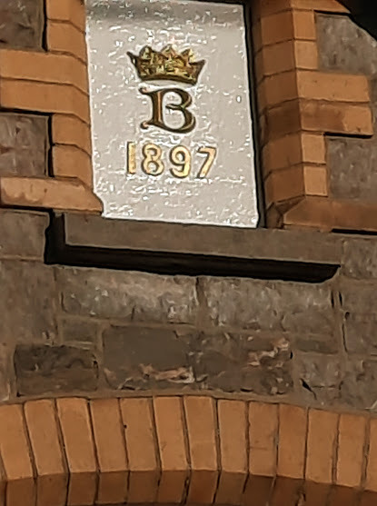 A picture of a plaque showing a crown, a capital B and the year 1897 inset into a brick wall